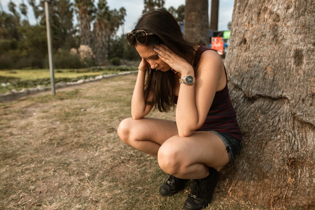 woman squatting in a park with a worried face holding her head with her hands